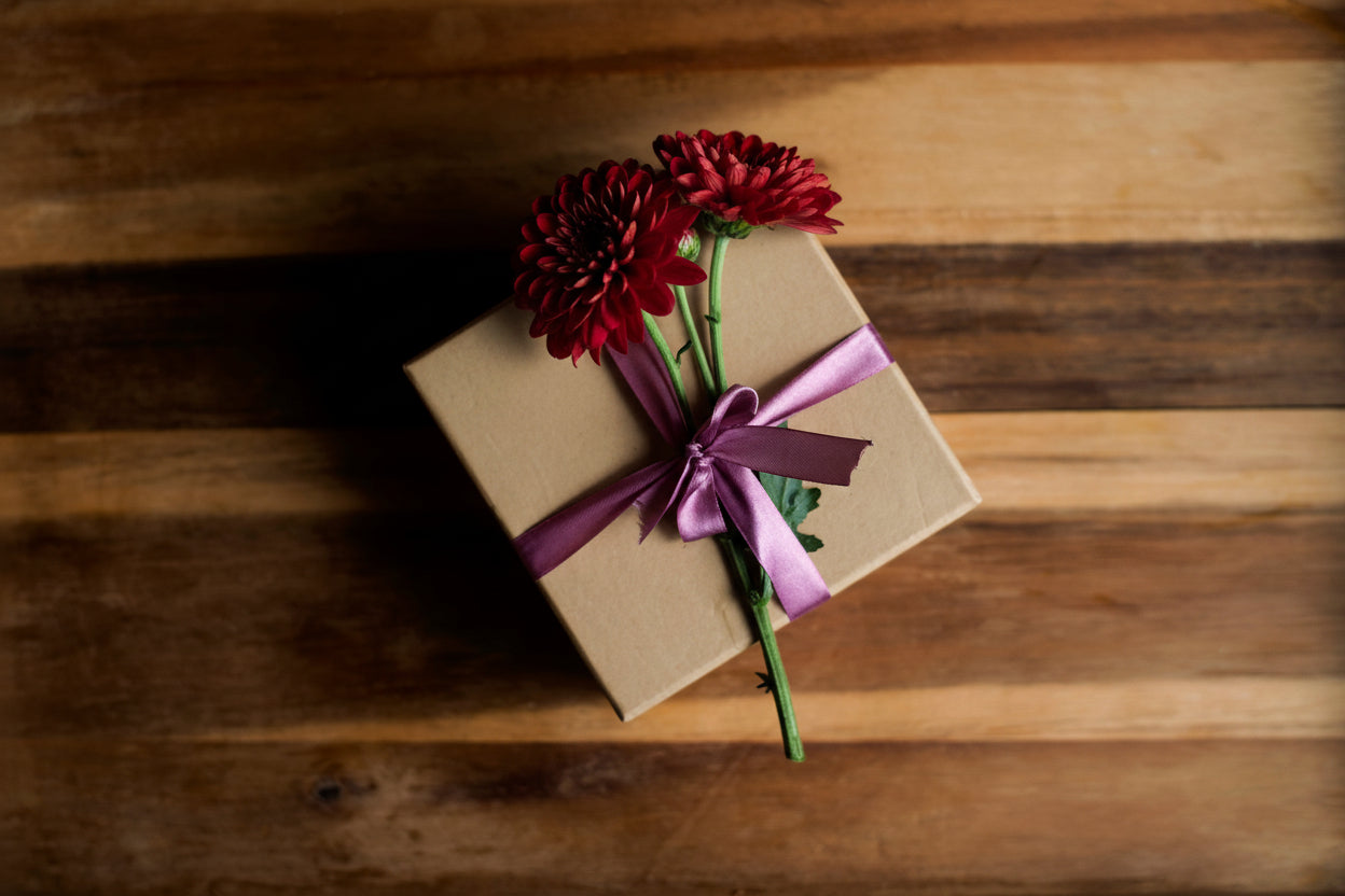 Gift box with a purple ribbon and white flowers on a wooden surface